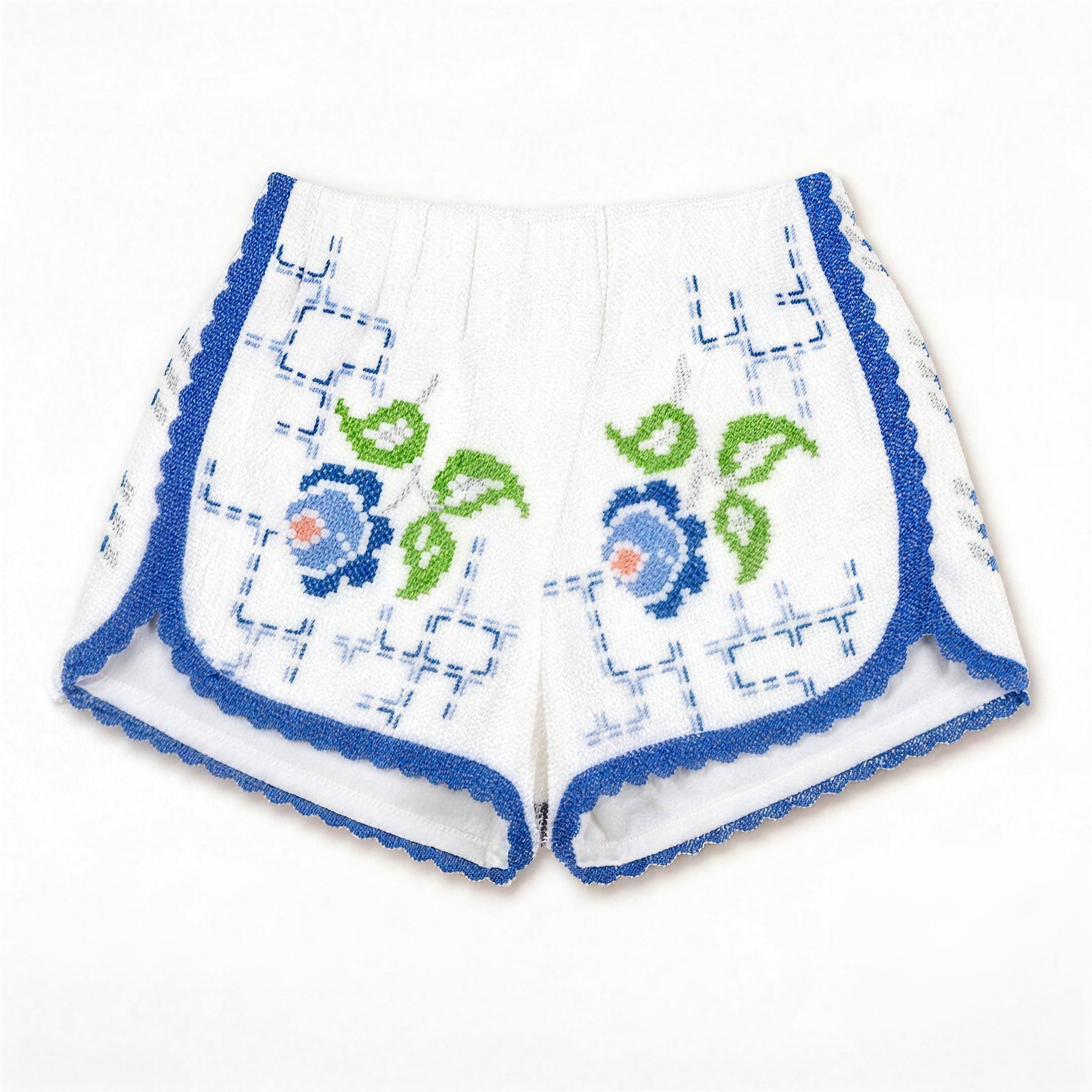 Shorts Verzura I DELAMIA — foglie verdi e fiori blu e corallo su bianco, vista frontale