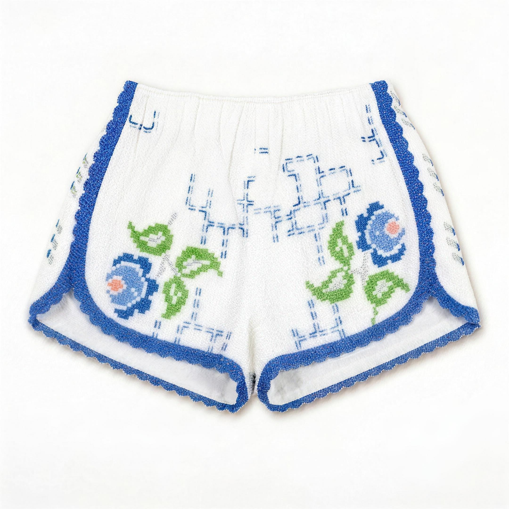 Shorts Verzura II DELAMIA — foglie verdi e fiori blu e corallo su bianco, vista frontale